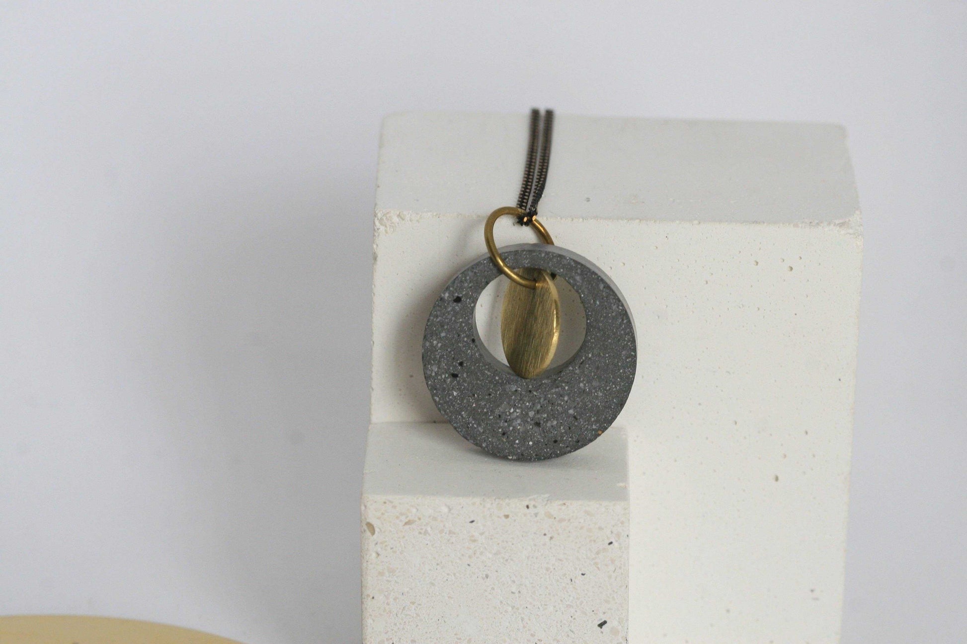 Beton ketting met gouden accent, op witte blok, minimalistisch en uniek