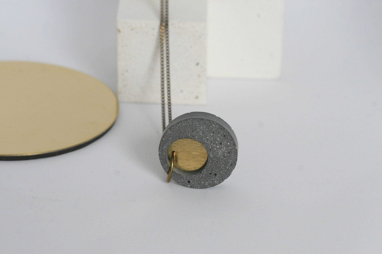 Beton ketting met gouden ring, op witte ondergrond, modern en tijdloos design